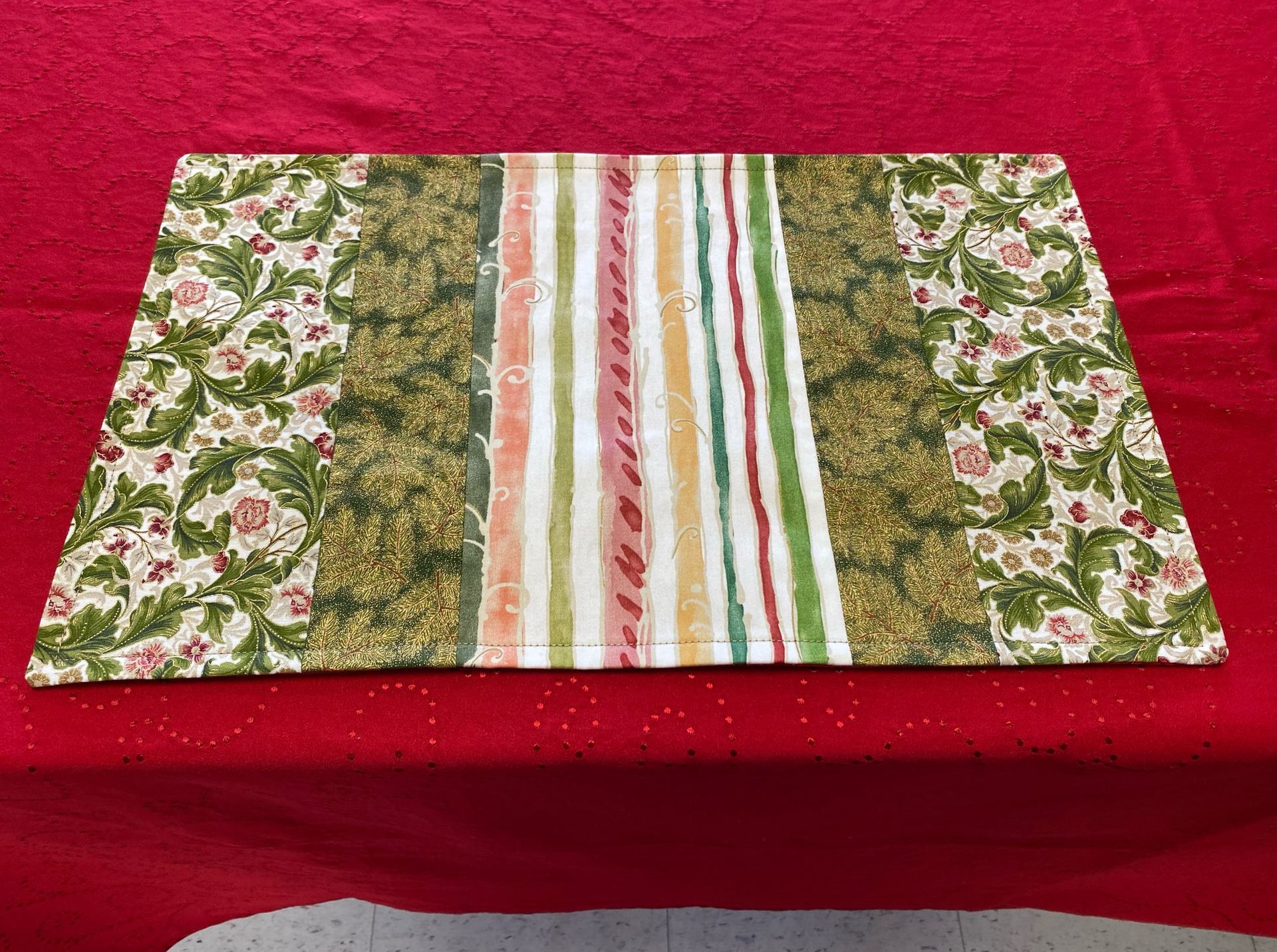 Floral fabric table runner with green and white striped center on a red background