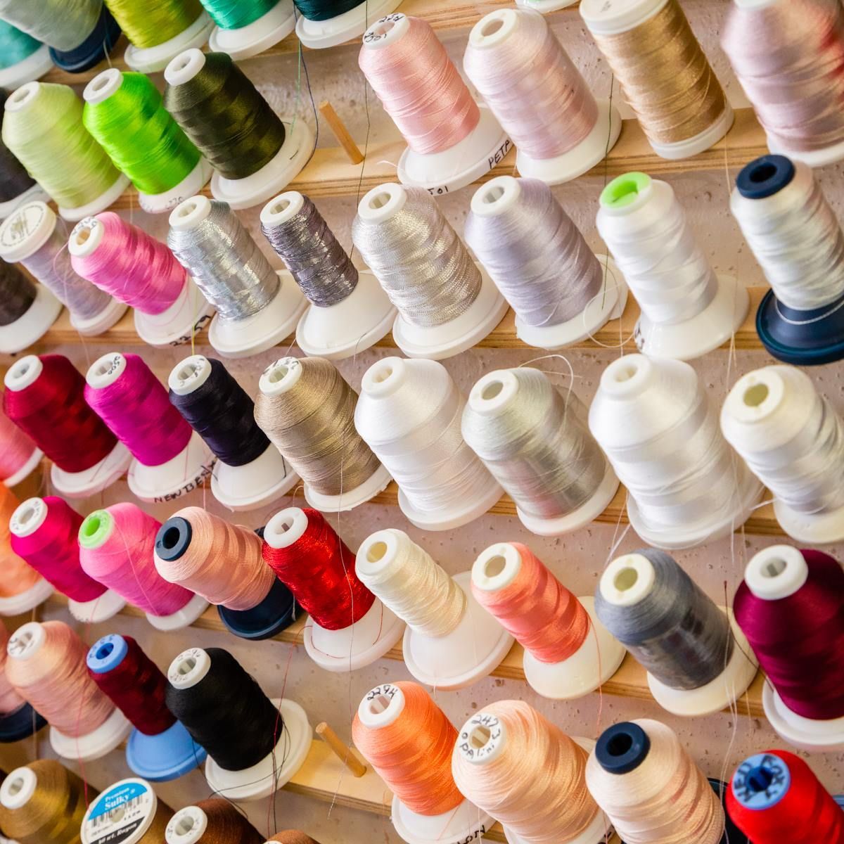 Colorful spools of thread arranged in rows on shelves, showing many shades from white to pink, green, and red