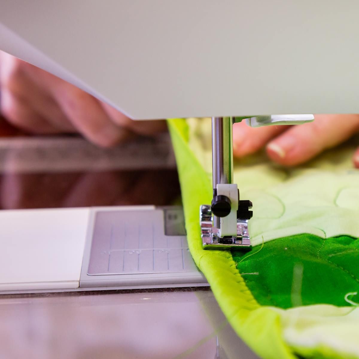 Hands sewing bright green fabric on a sewing machine close-up