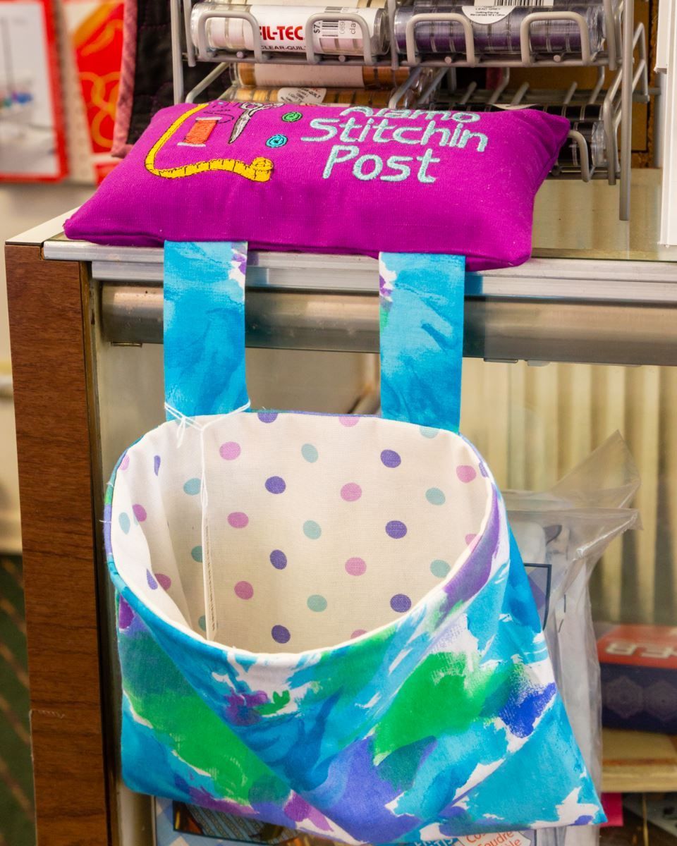 Colorful hanging fabric pouch with polka dots and blue straps, displayed on a store rack.