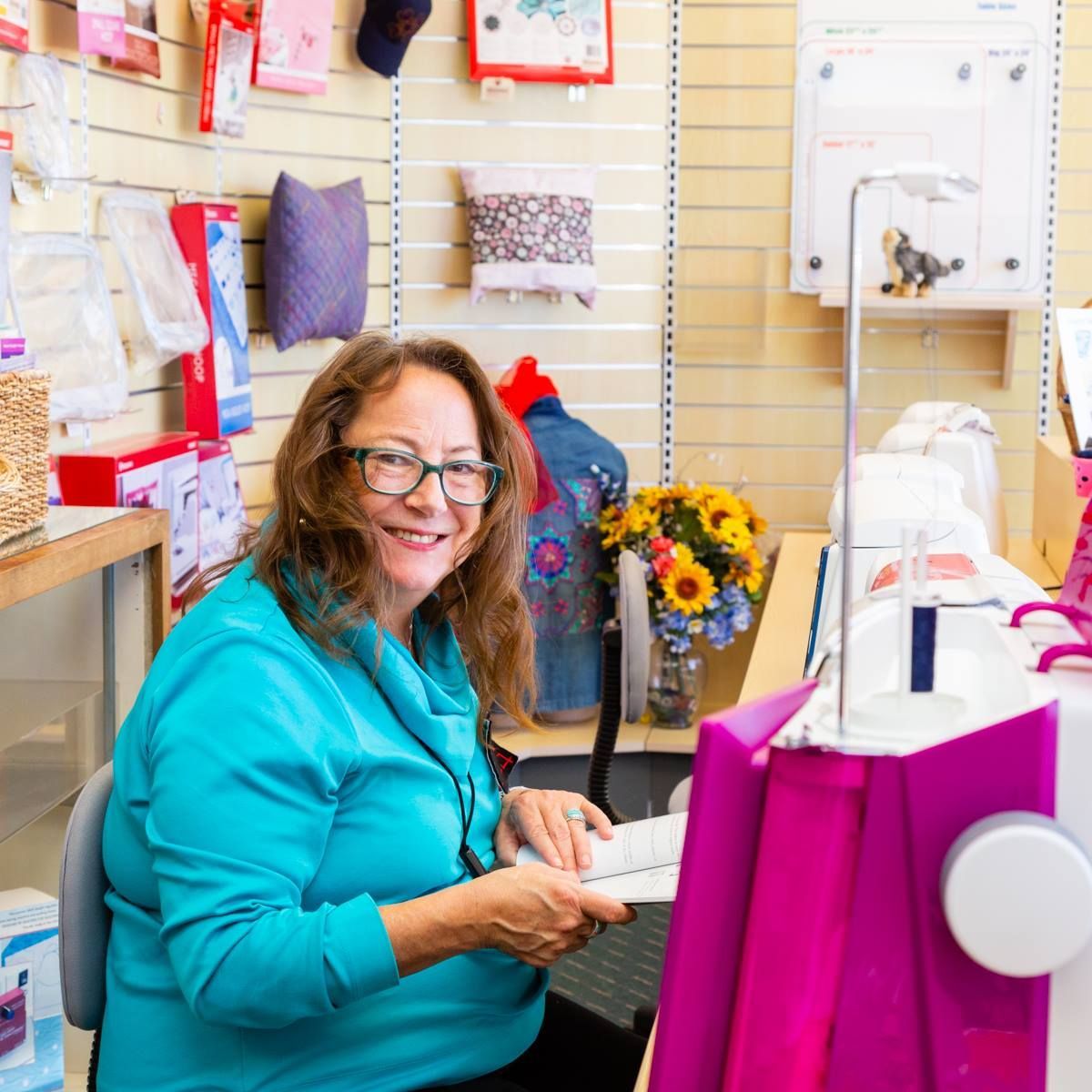 Woman in teal shirt smiling at a sewing machine in a fabric shop