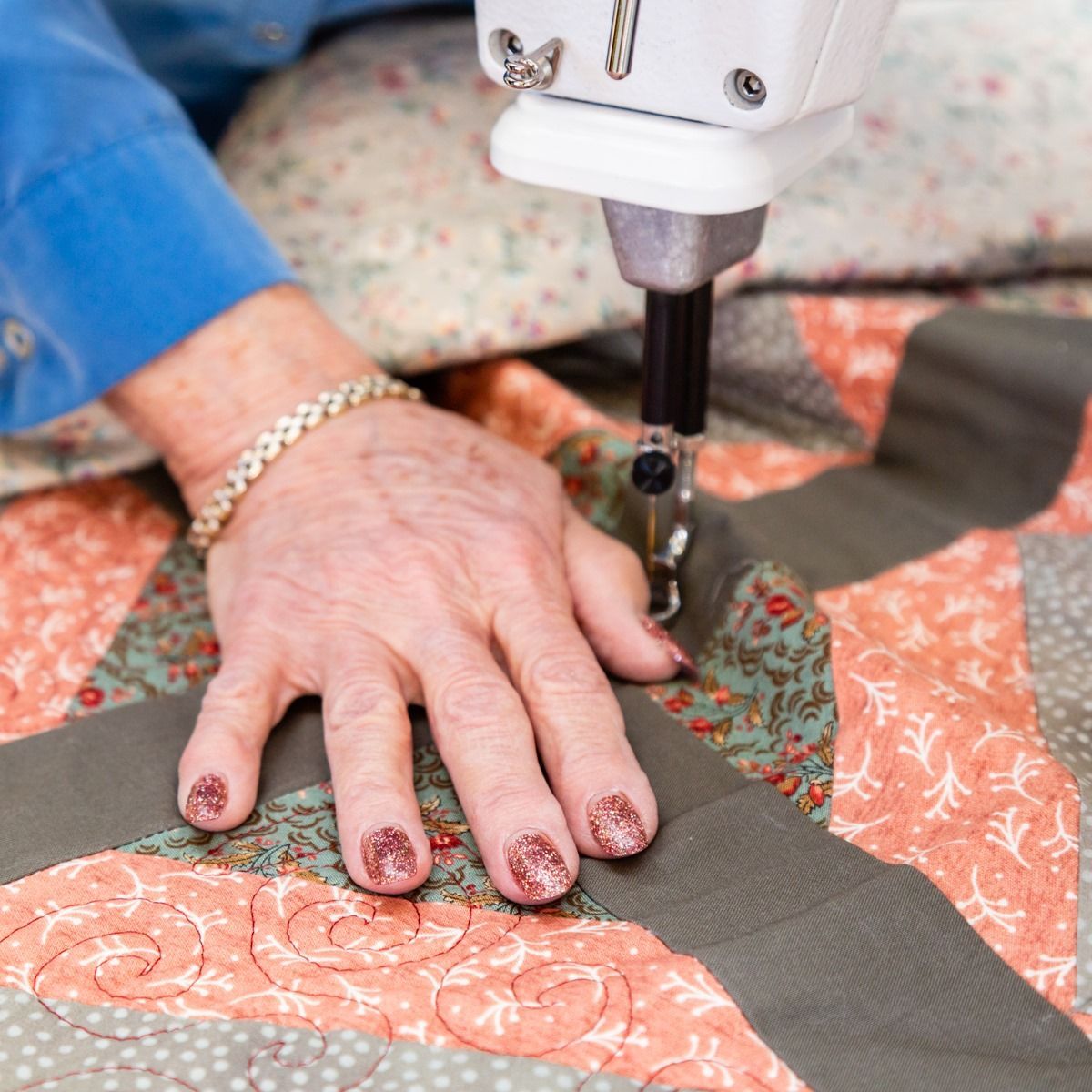 Hand guiding fabric under a sewing machine, quilting a gray strip on coral patterned cloth.