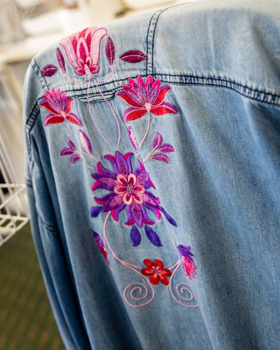 Embroidered pink and purple floral design on the back pocket of blue denim jeans