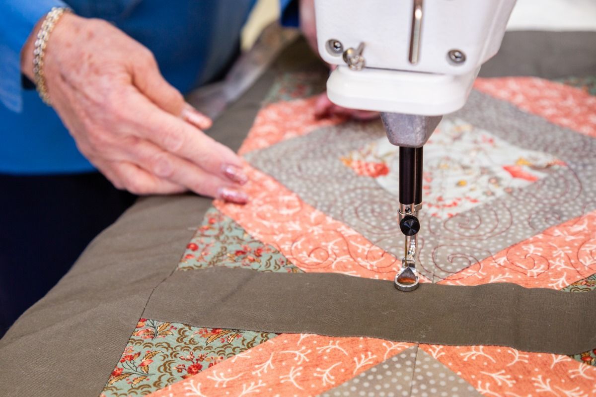 Hand guiding a sewing machine stitching a quilt with coral and floral fabric patches