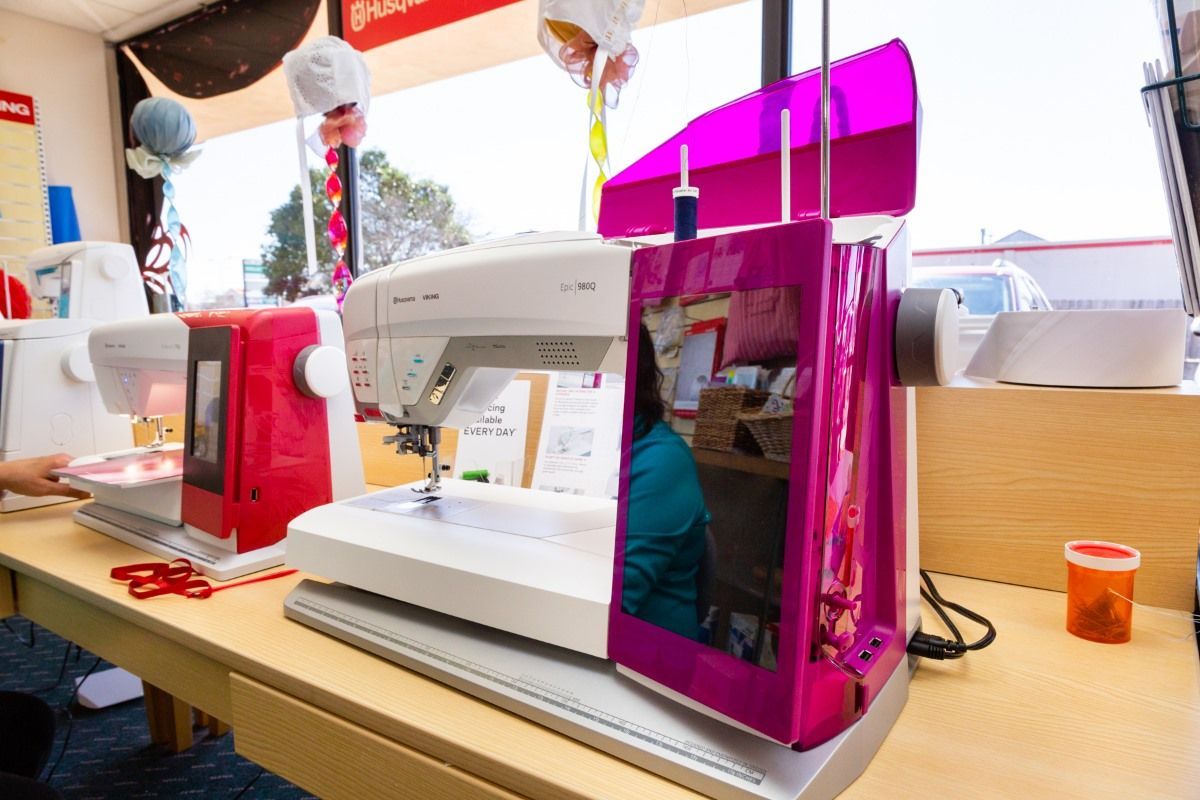 Two sewing machines on a table, one white and one pink, in a bright craft room
