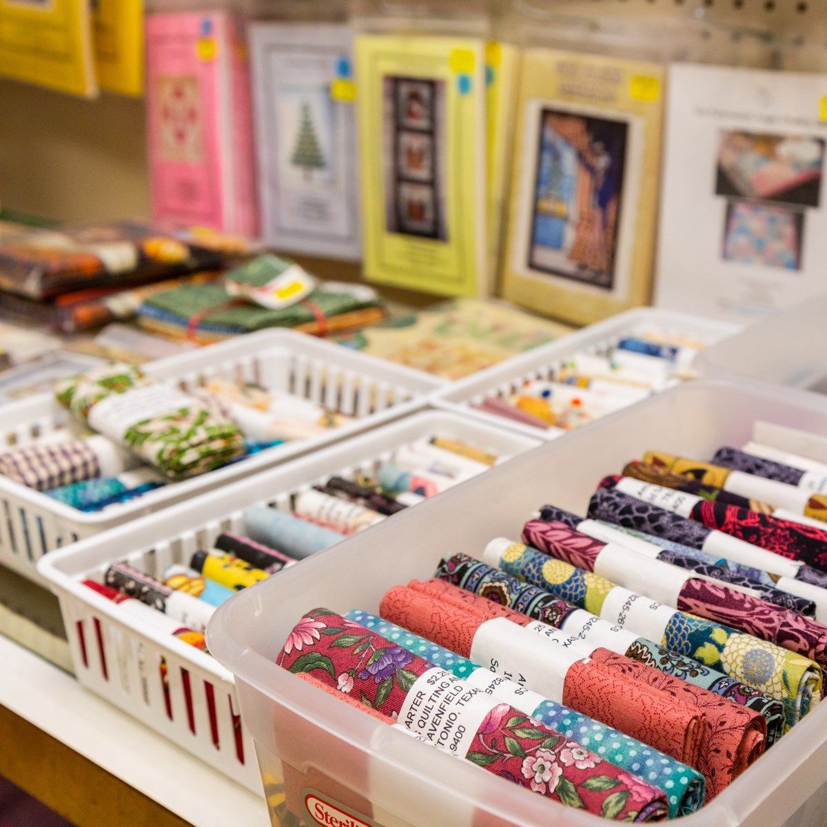 Trays of colorful sewing supplies and patterned fabric rolls on a store table