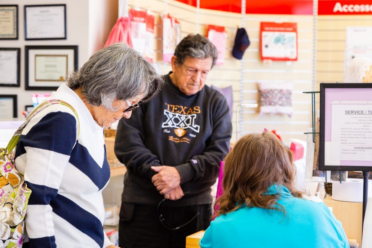 Two people talking with a seated person at a service counter in a bright office setting