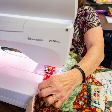 Hands sewing red-and-white fabric on a white Husqvarna Viking sewing machine