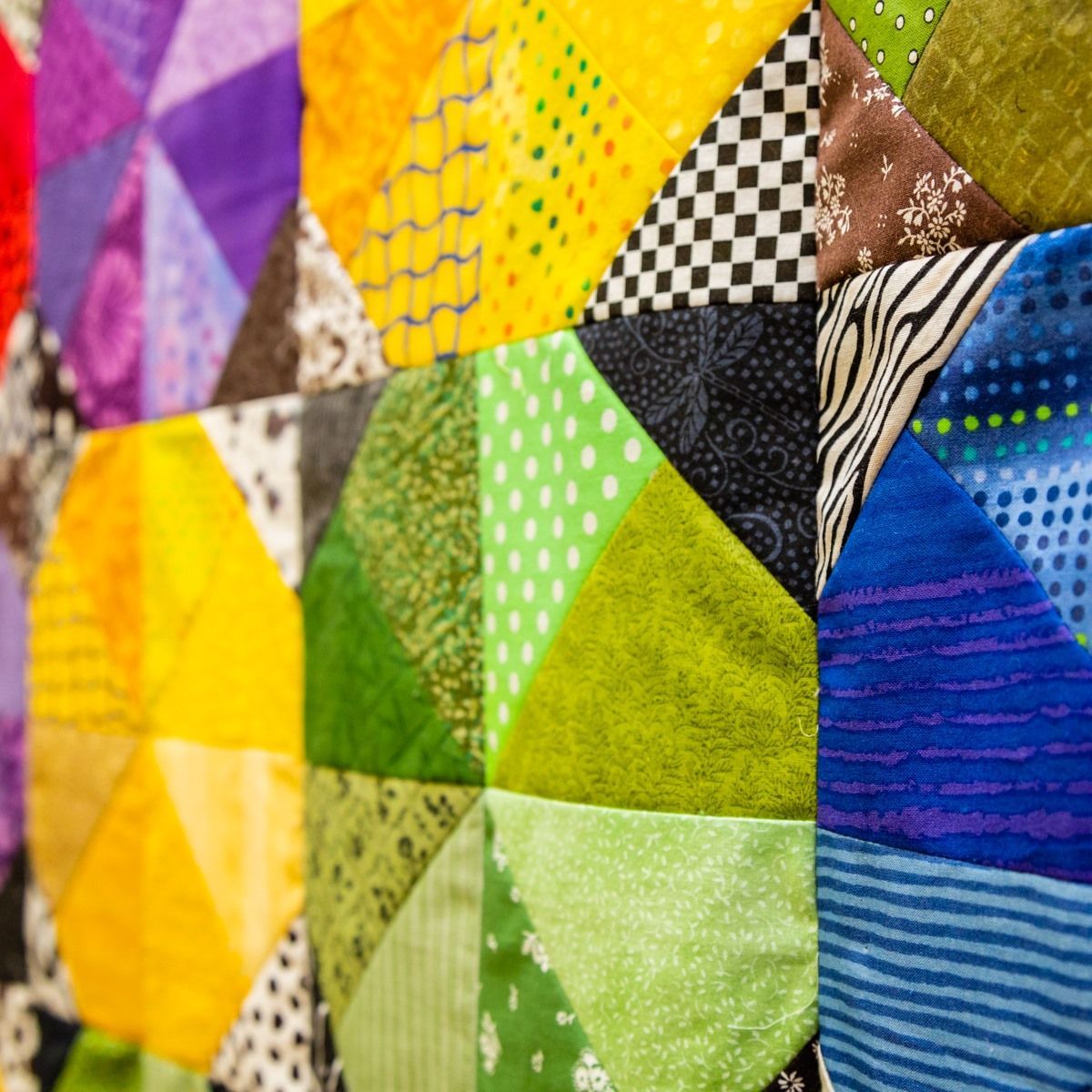 Colorful patchwork quilt with geometric triangles and patterns in bright yellow, green, blue, and brown