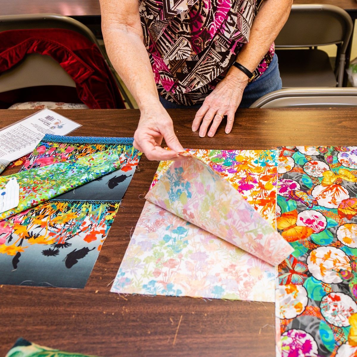 Hands arranging colorful patterned fabric swatches on a table