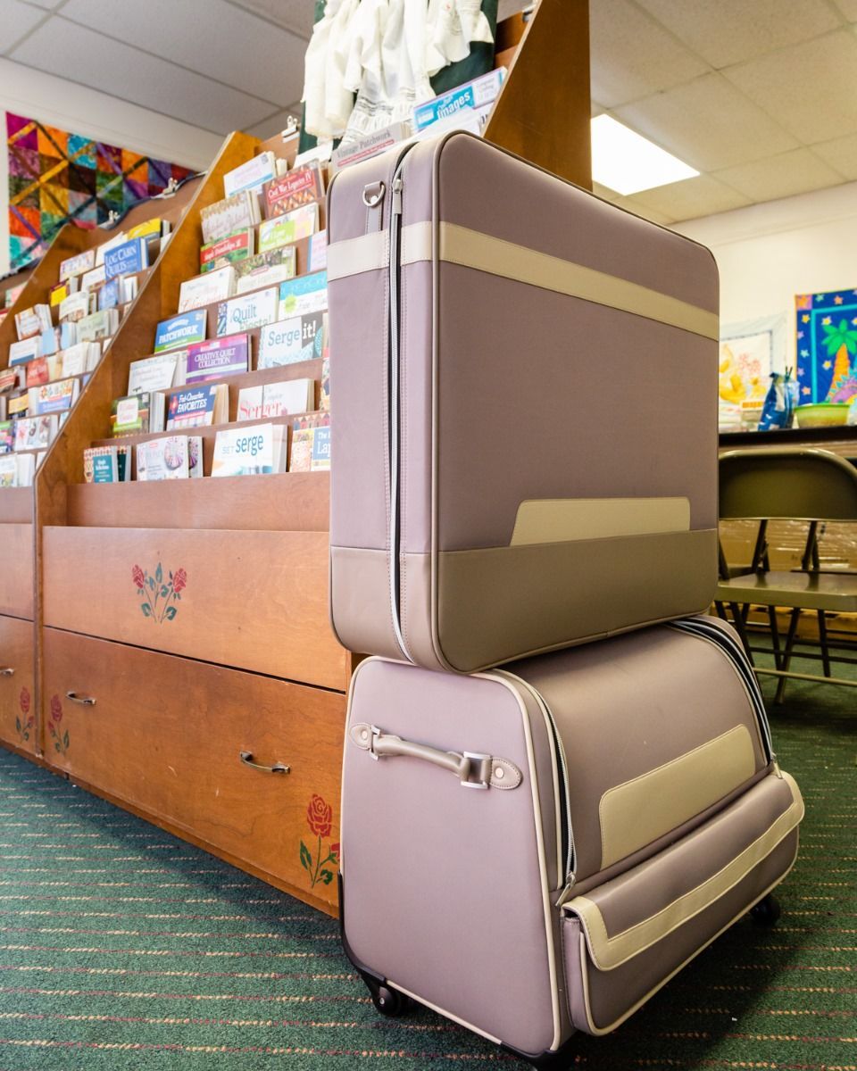 Stacked pink suitcases beside a wooden display in a library or classroom.