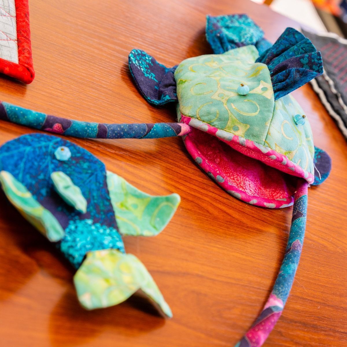 Colorful handmade fabric fish ornaments on a wooden surface, with blue, green, and pink patchwork patterns