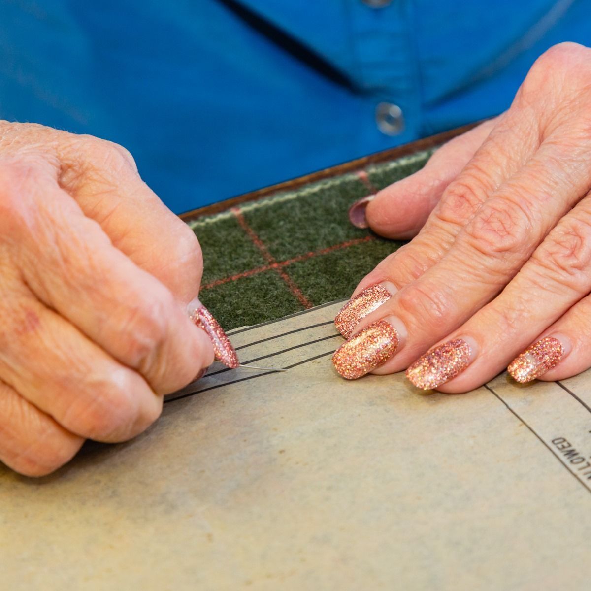 Hands using a ruler and pencil to measure fabric on a worktable