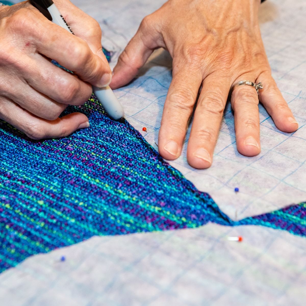 Hands pinning blue fabric while tracing a pattern on a quilt.