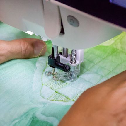 Close-up of hands guiding green fabric under a sewing machine needle.