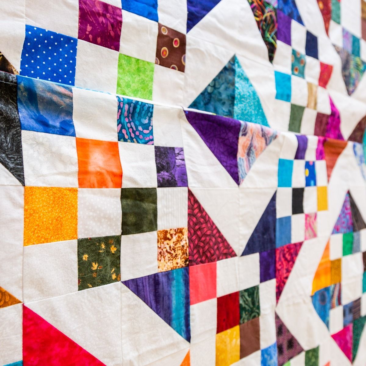 Colorful patchwork quilt with geometric fabric squares and triangles in blue, purple, orange, red, and white