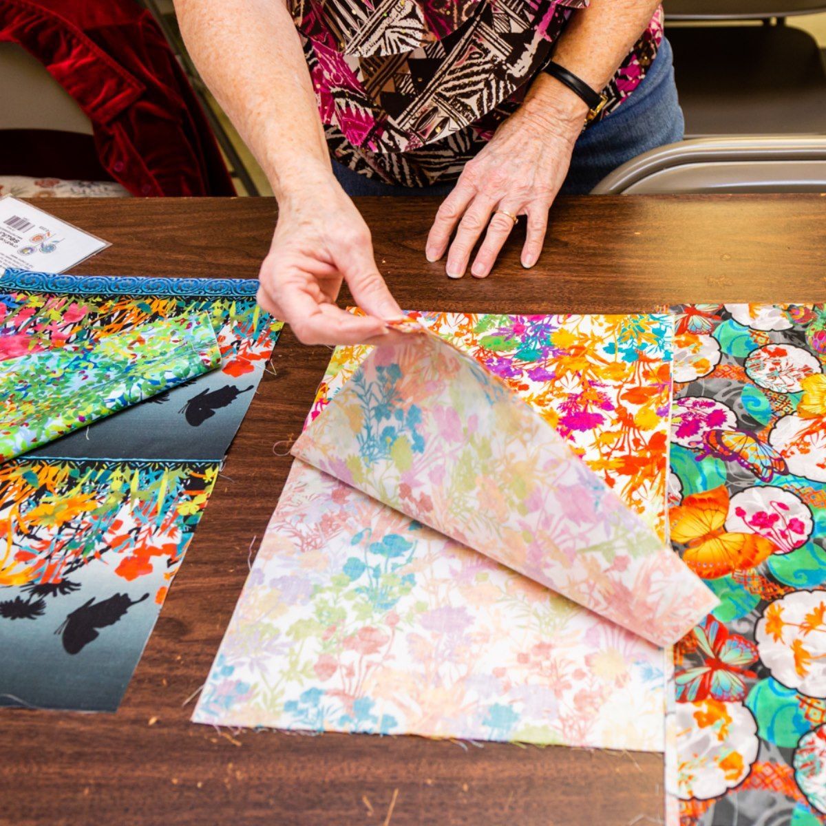 Hands arranging colorful patterned fabric swatches on a wooden table