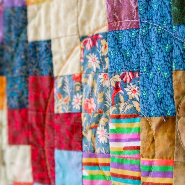 Colorful patchwork quilt with floral and striped fabric squares in red, blue, yellow, and pink