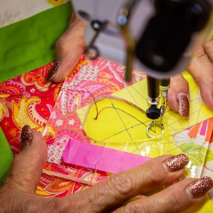 Hands sewing colorful fabric patchwork with a sewing machine.