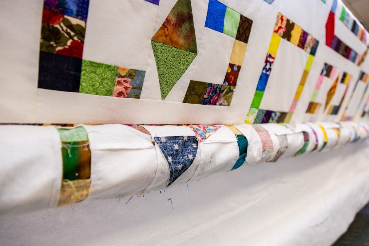 Colorful quilt squares sewn along a white fabric railing in a bright indoor hallway