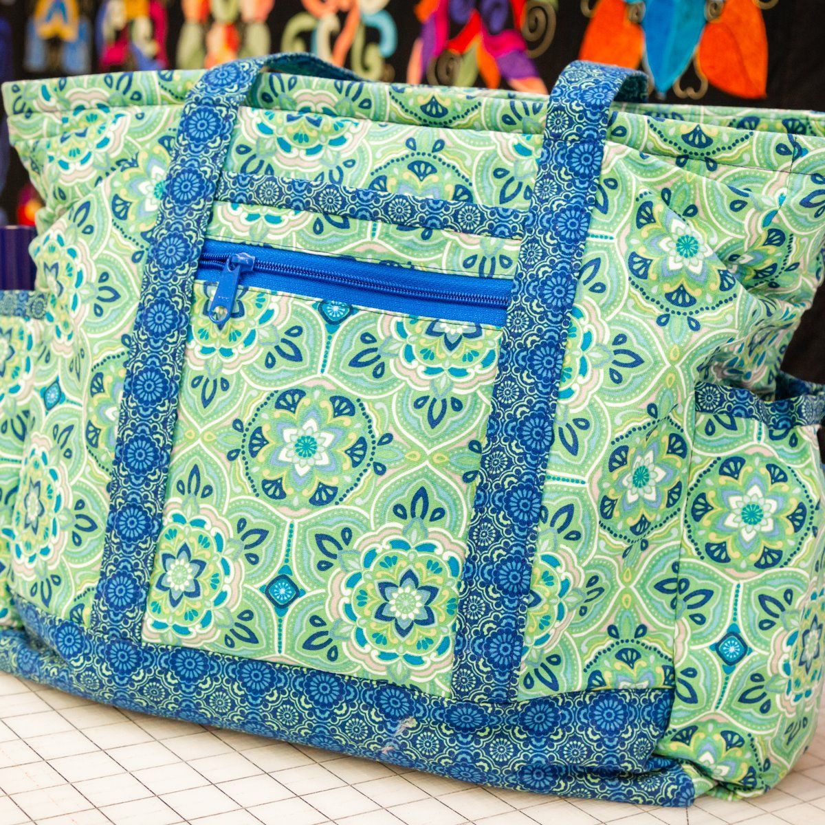 Blue and green patterned tote bag with long handles on a tiled surface.