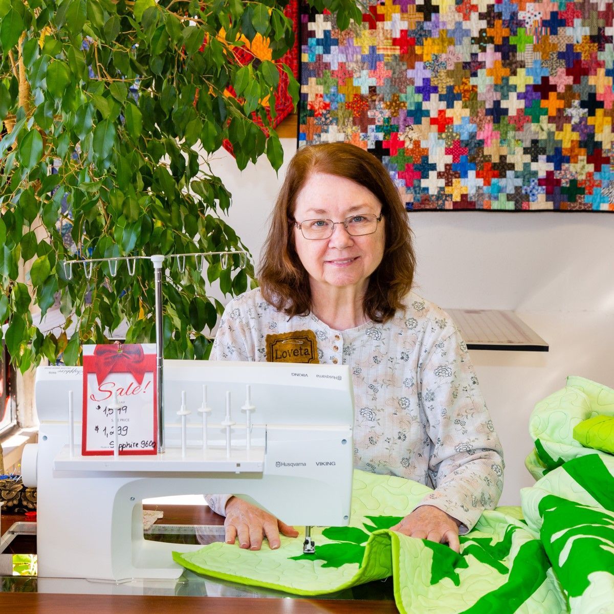 Woman at a sewing machine with colorful patchwork and green fabric in a bright craft room