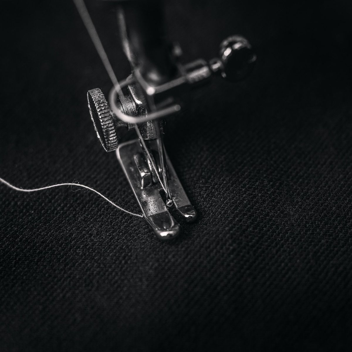 Close-up of a sewing machine presser foot stitching white thread on black fabric