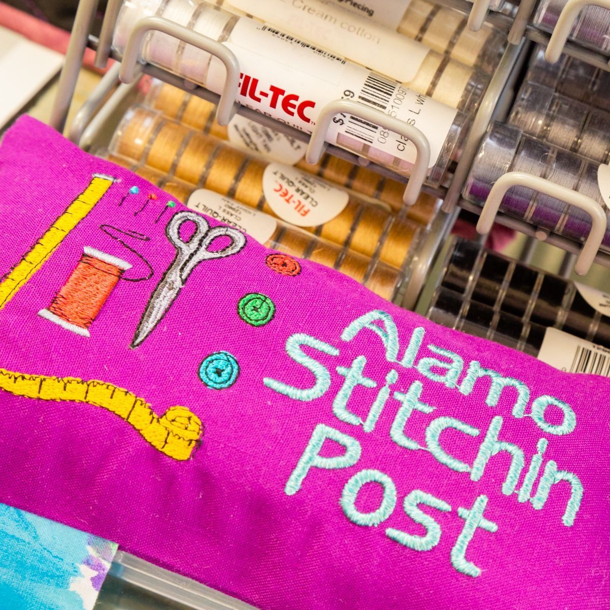Pink Alamo Stitchin Post embroidery with scissors and thread cones in a sewing machine