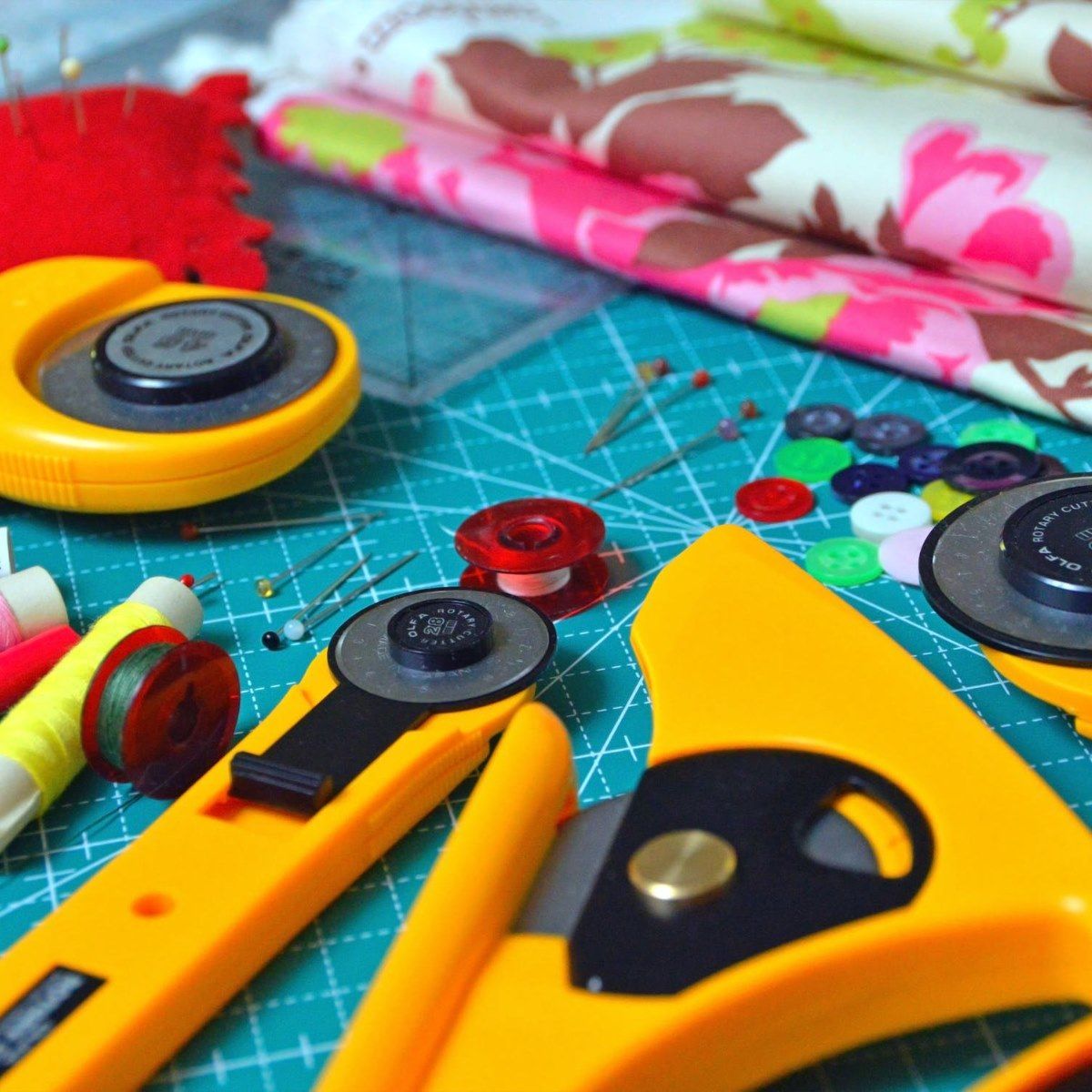 Cutting tools, thread, and colorful fabric on a sewing mat with pins and notions