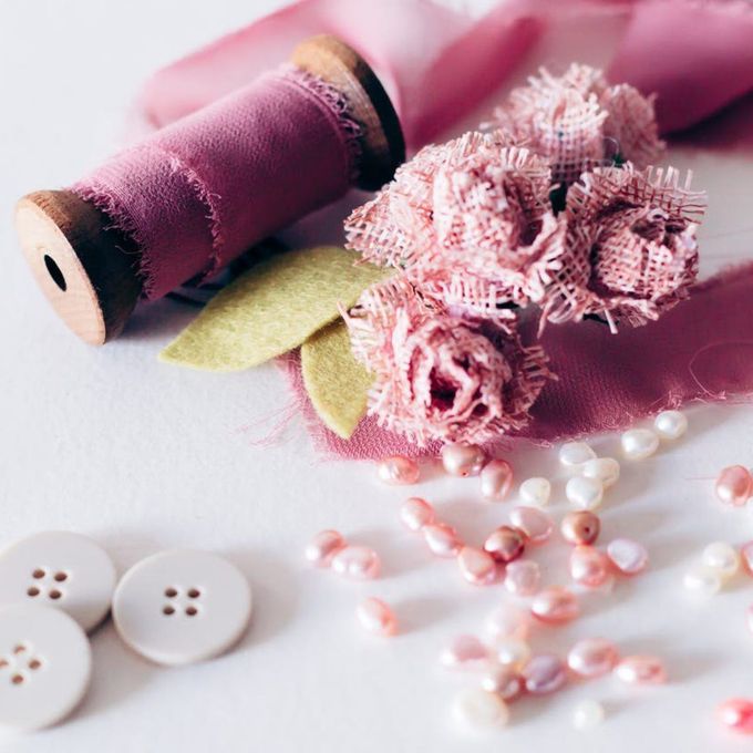Pink thread spools with lace flowers, buttons, and pearl beads on a white surface.