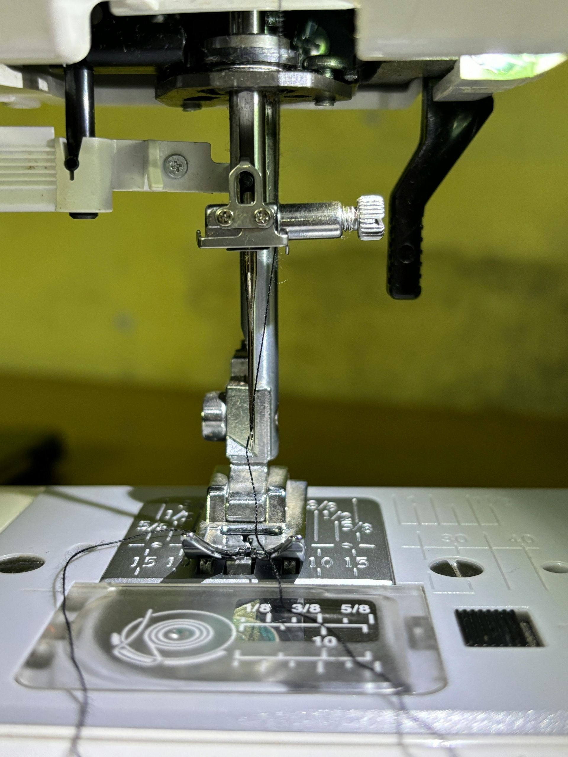 Close-up of a sewing machine needle and presser foot stitching black fabric on a white machine