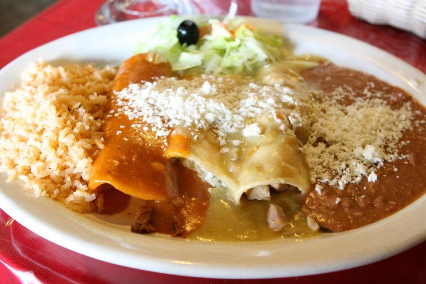 Plate of enchiladas, rice, and beans, topped with cheese.