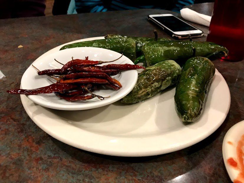 Plate of green and red peppers on a table. Small white bowl with red peppers. Cellphone visible.