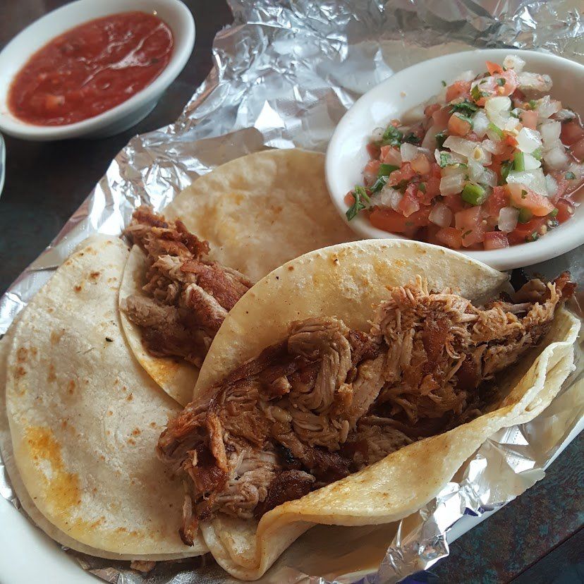Two tacos filled with shredded meat, salsa, and pico de gallo served with red salsa.