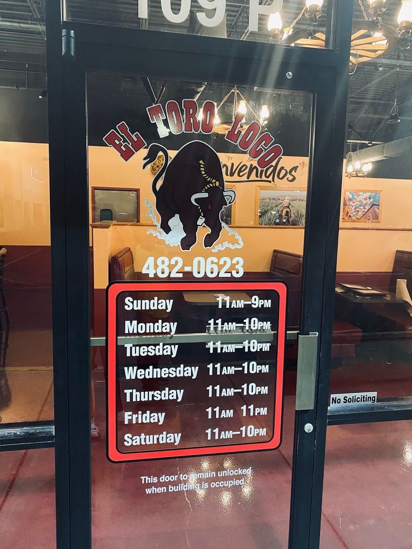 A restaurant door with a bull logo, hours, and phone number.
