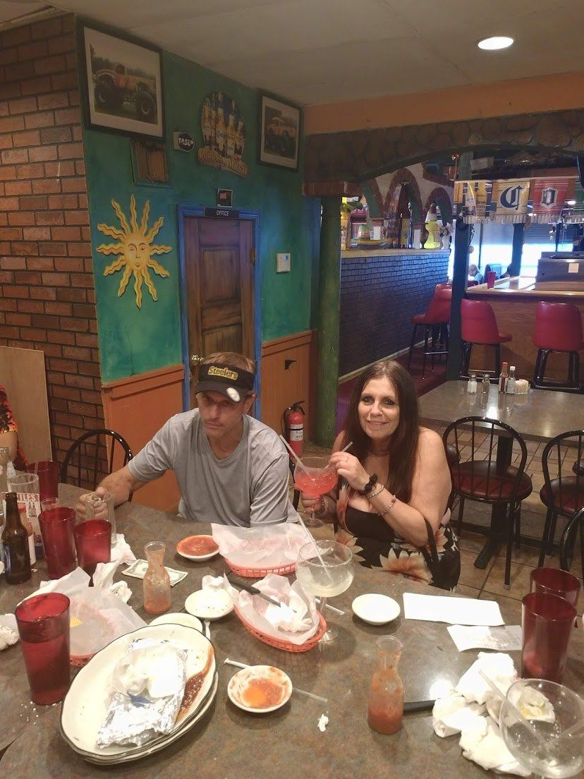 People seated at a table in a Mexican restaurant, eating and drinking. Colorful walls and decor are visible.