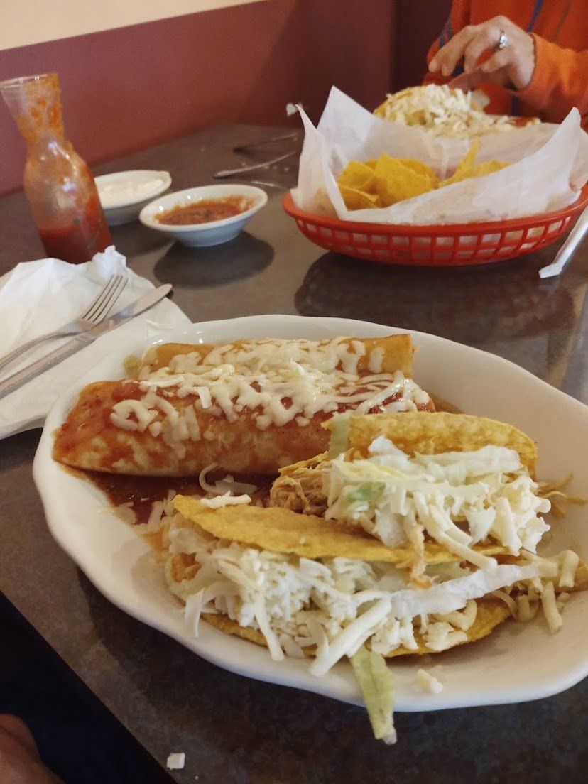 Plate of enchiladas and tacos, with a basket of chips and salsa on a table.