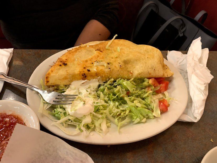 Large, grilled quesadilla with lettuce, tomato, and sour cream on a white plate. Salsa in a small bowl.