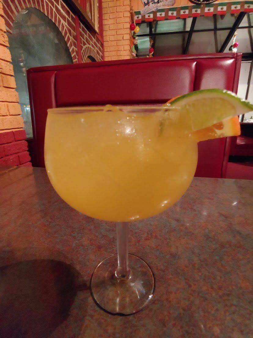 Orange cocktail in a large stemmed glass with orange and lime garnish.