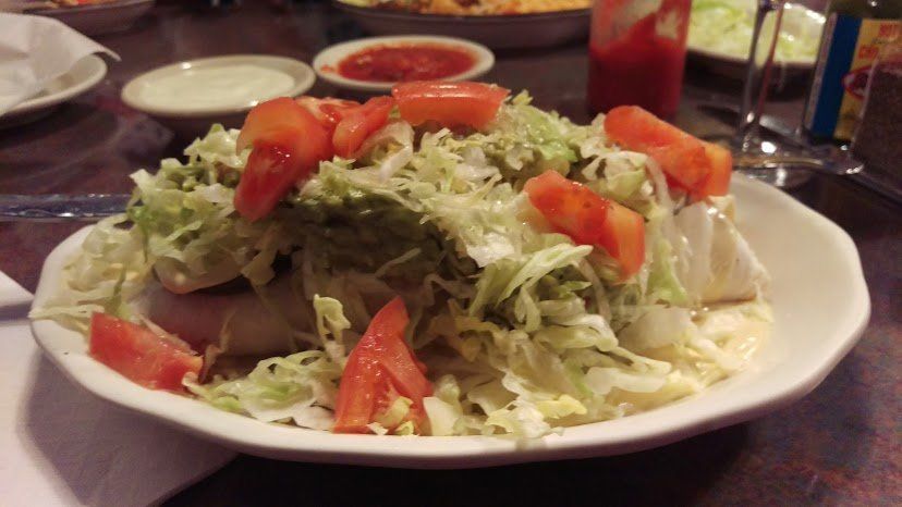 Enchilada plate with shredded lettuce, tomatoes, and side dishes of salsa and sour cream.