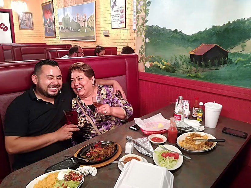 Two people, smiling, seated at a restaurant table with food, drinks, and decor.