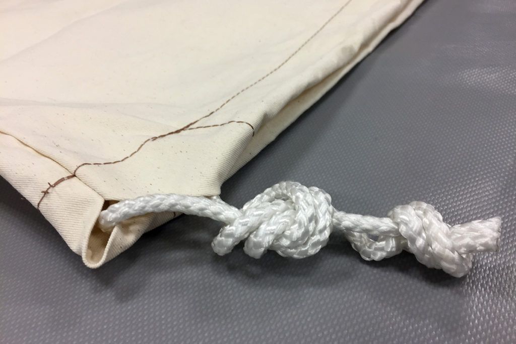 Close-up of a white fabric bag with a drawstring and knot closure.