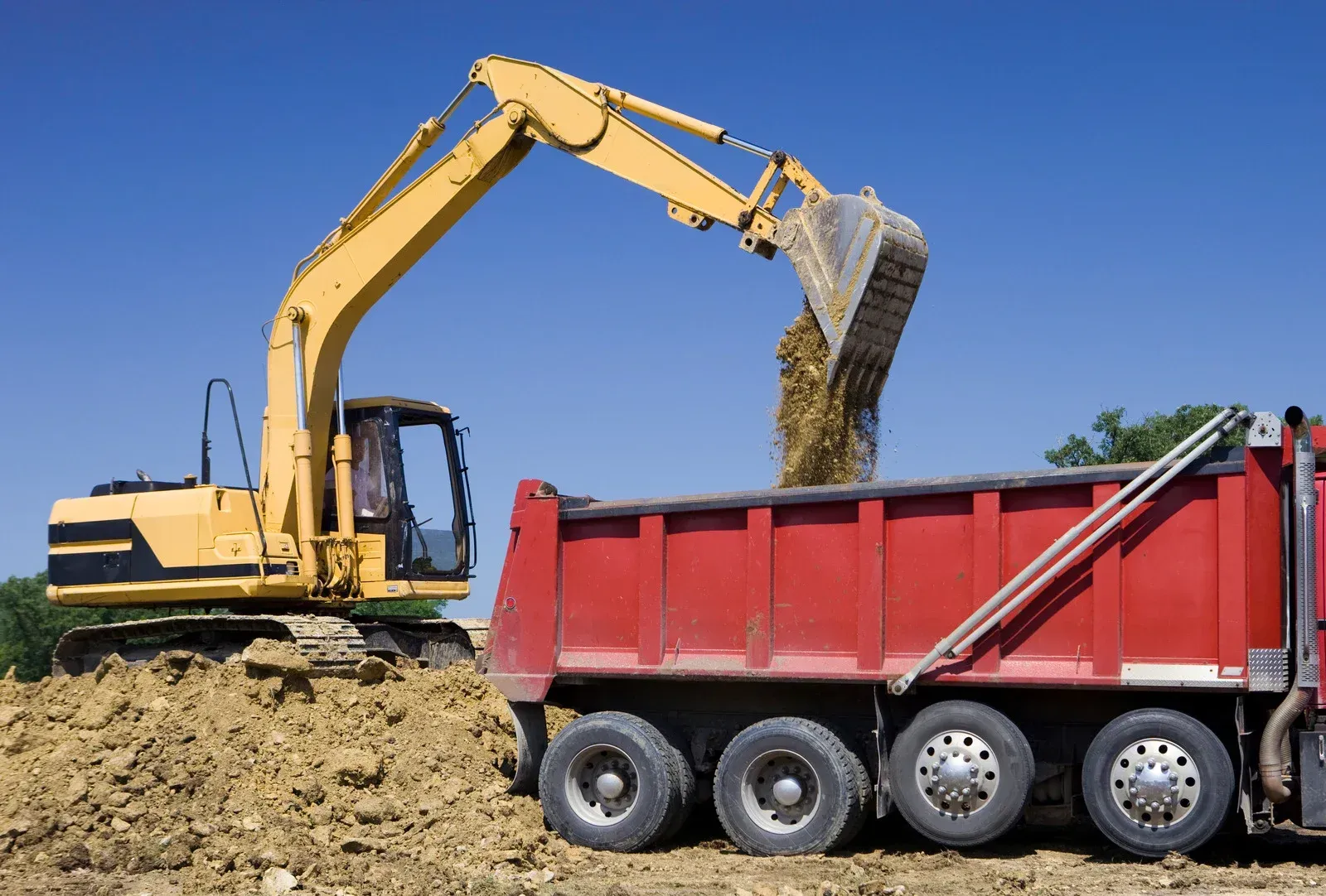 A yellow excavator is loading dirt into a red dump truck.