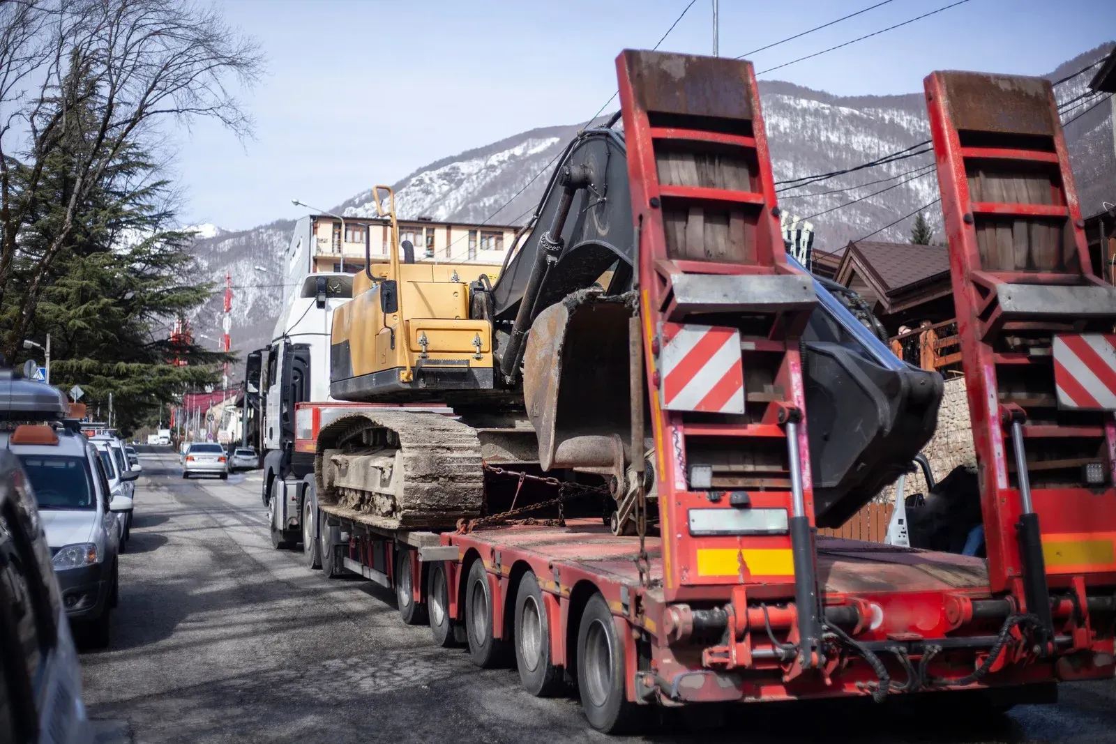 A red and yellow truck is carrying a large excavator on a trailer.