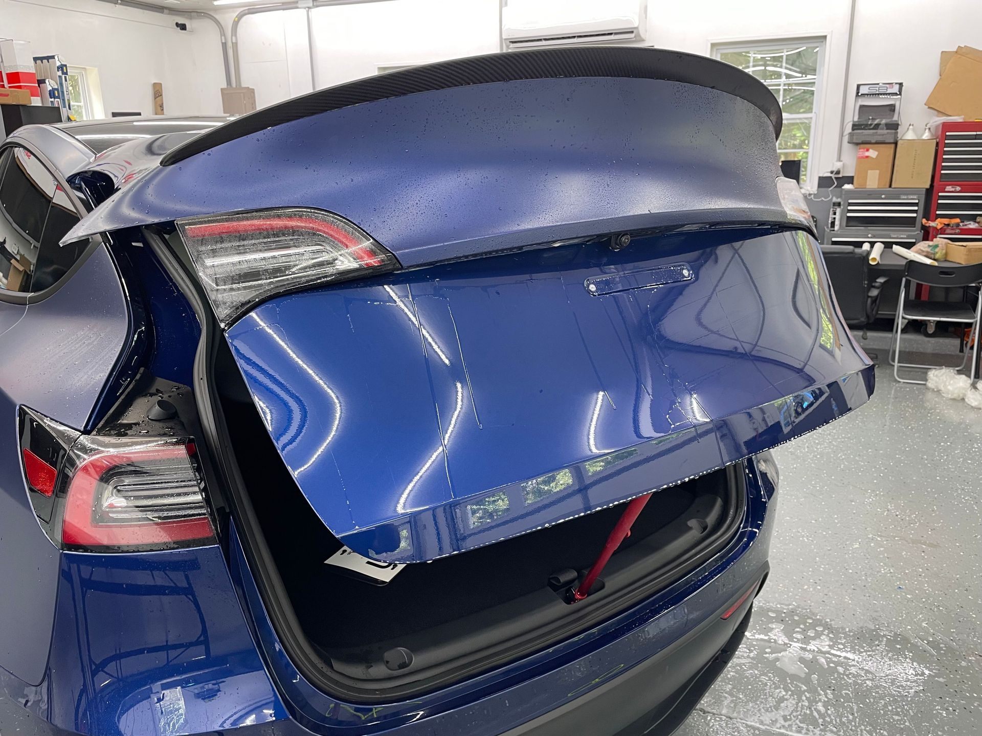 Blue Tesla Model 3 with open trunk, in a workshop setting.