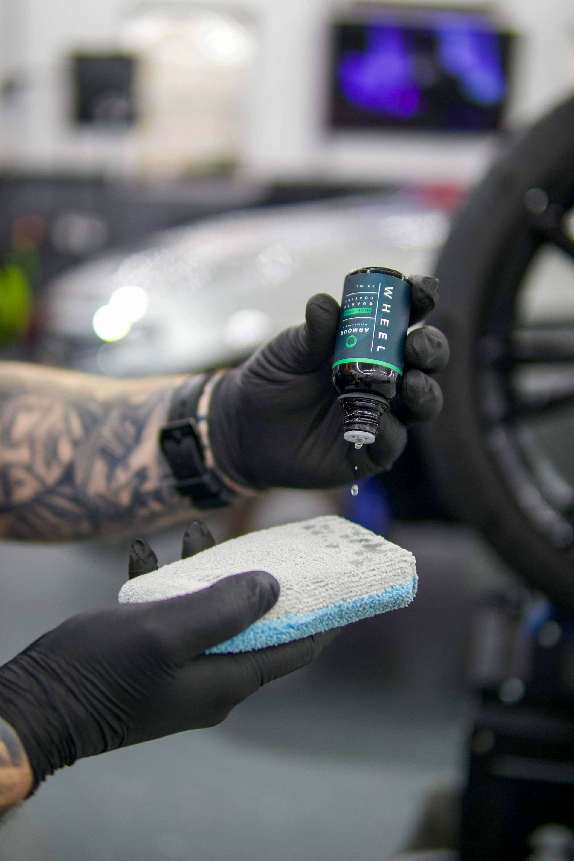 A person in black gloves applying detailing product from a bottle onto a sponge in a shop.