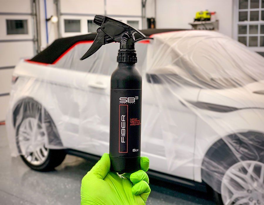 Person holding black spray bottle in front of a white car covered in plastic wrap.