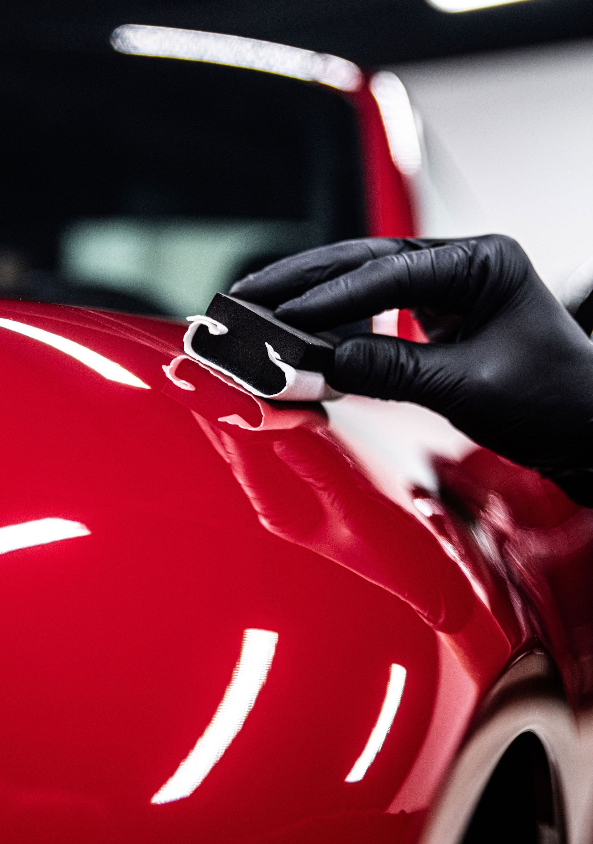 Gloved hand applying a ceramic coating to a shiny red car.