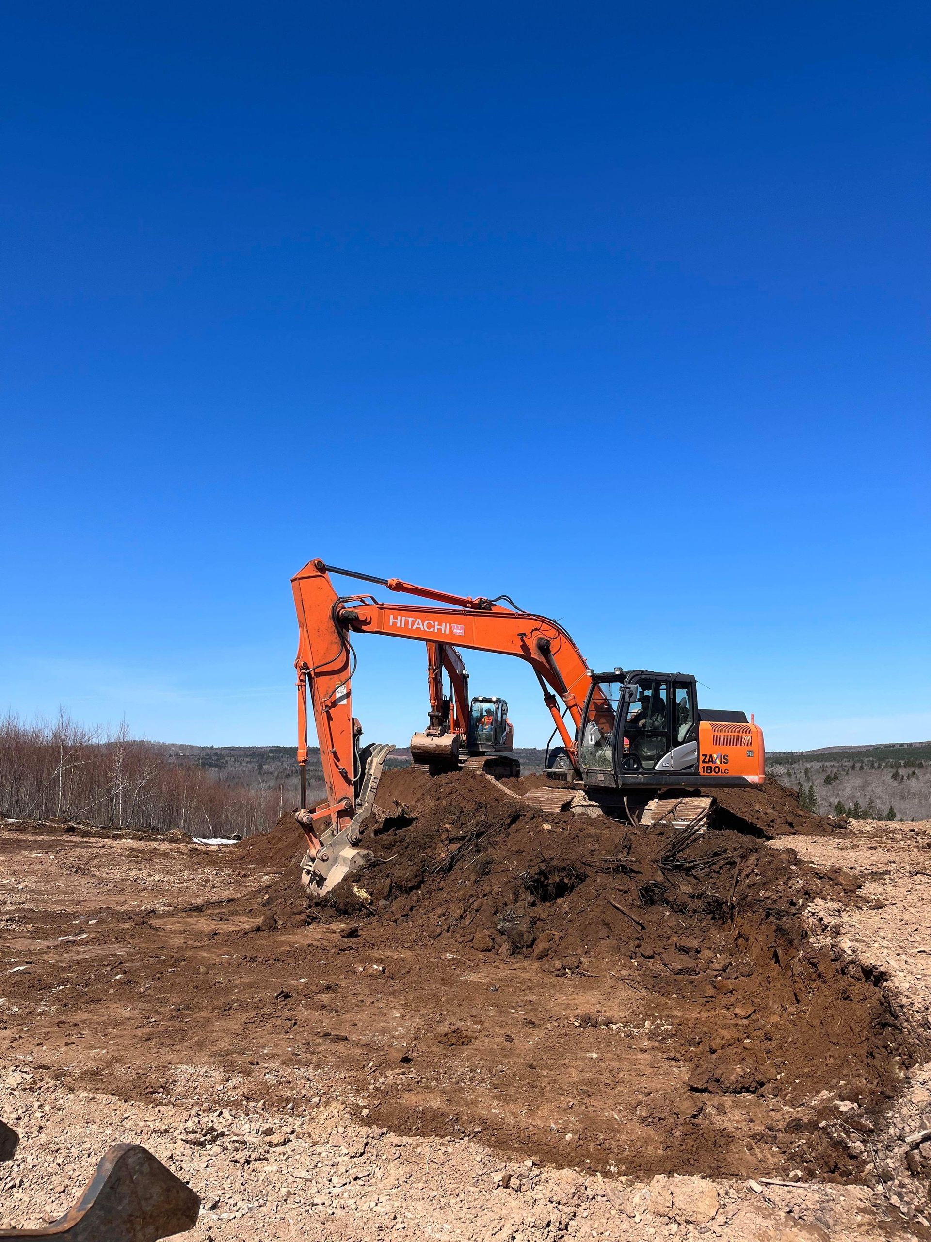 A large orange excavator is digging a hole in a dirt field.