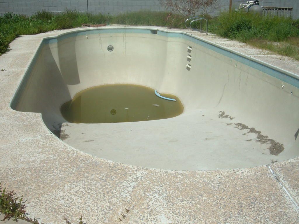 Empty abandoned swimming pool with cracked concrete and a small puddle of greenish water